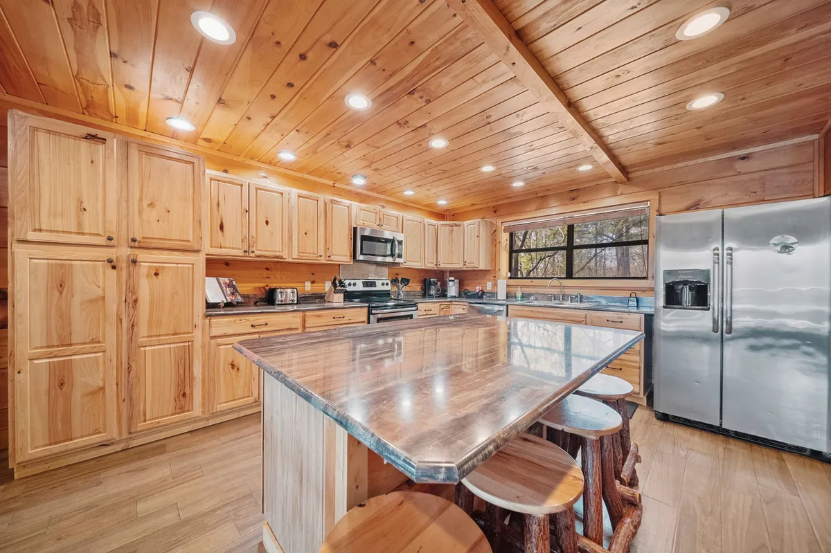 Bright and welcoming, this kitchen highlights a central island, gleaming stainless steel appliances—including a double-door refrigerator—and abundant natural light from large windows. The cabinetry and spacious layout support easy group meal prep and casual interaction.
