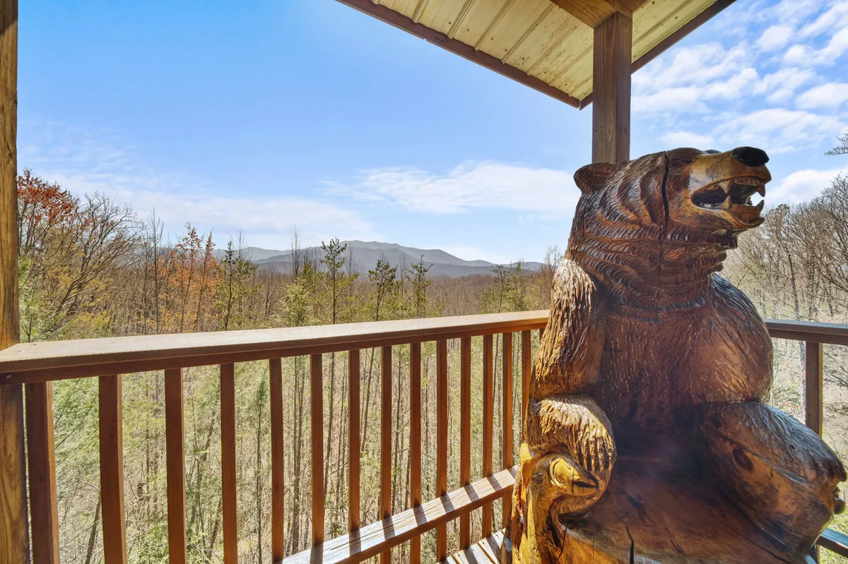 A wooden bear sculpture on a deck with a backdrop of wide mountain vistas and sturdy railing, emphasizing the connection to nature and offering a whimsical, family-friendly touch.