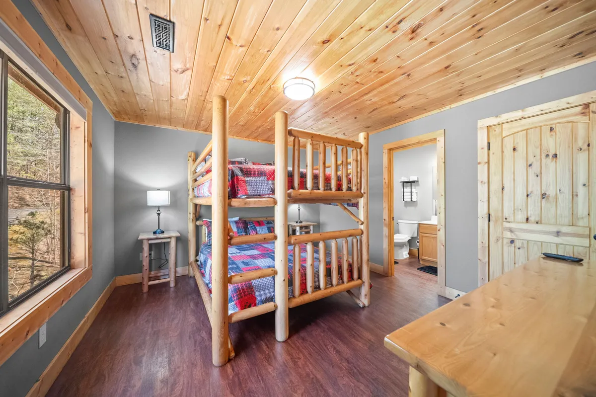 A playful and inviting bunk bedroom with a sturdy bunk bed, wooden furniture, a window that lets in natural light, and a bedside lamp. The setting is ideal for children or friends, offering a cozy and communal atmosphere for relaxation, games, or bedtime stories.