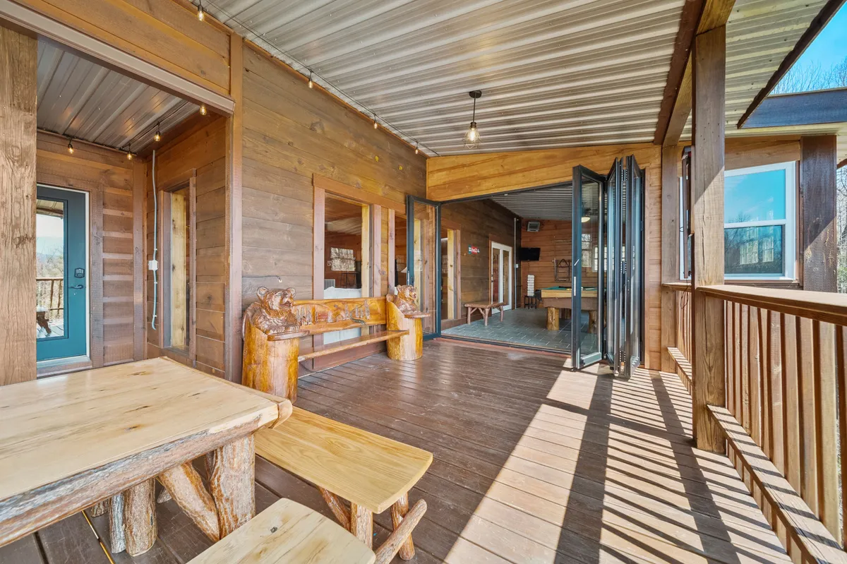 A cozy outdoor dining area surrounded by wooden sculptures and open doors, inviting guests to dine or socialize outside. The space glows warmly, evoking the charm of sunset dinners or celebrations under the stars.