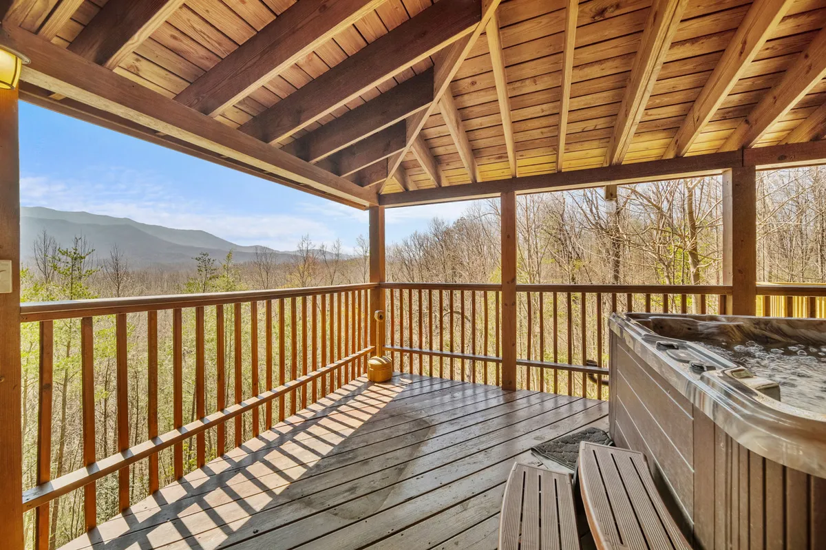 A peaceful wooden deck with an inviting hot tub overlooking the Smoky Mountains. The hot tub is positioned for prime views, surrounded by sturdy wooden railings and mountain scenery in the distance. The setting is tranquil, perfect for relaxing and soaking while admiring nature.