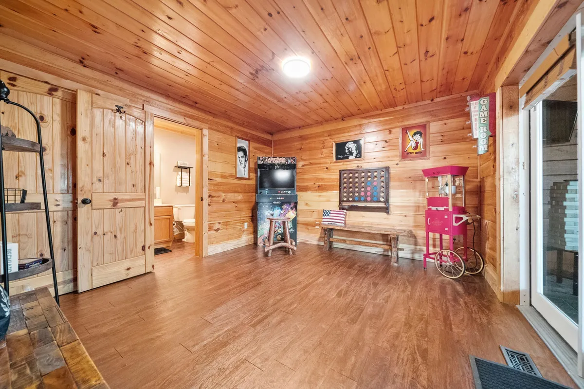 A cozy, wood-paneled entertainment space featuring a popcorn machine, framed art, wall-mounted television, and relaxed seating. The nostalgic touches and inviting setup evoke memories of movie nights and social gatherings centered around games and fun.