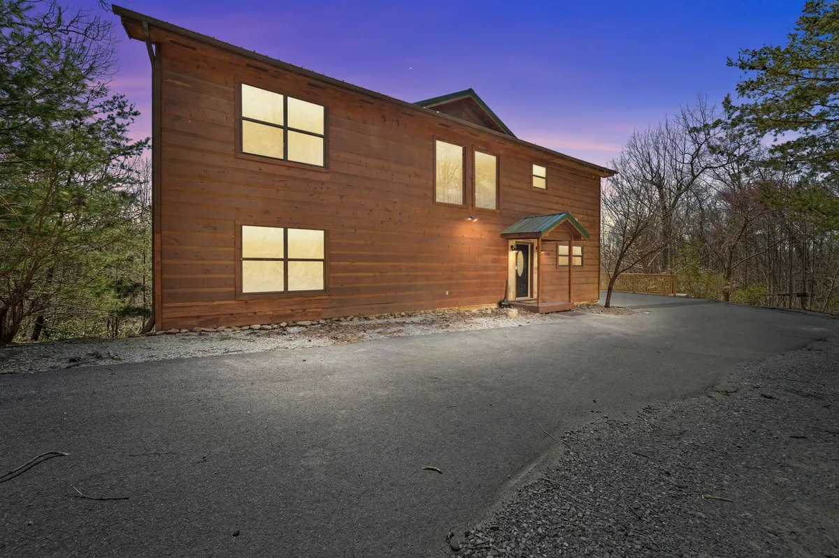 The inviting wooden exterior of the house, highlighted by large windows and a welcoming entryway with a small roof. The scene suggests a peaceful, private mountain setting with easy access to nature trails or porch relaxation.