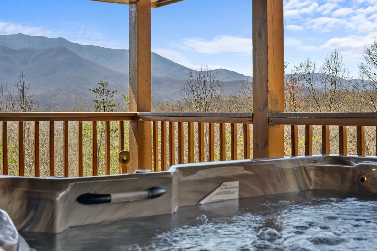 A serene exterior scene of a bubbling hot tub on a wooden deck overlooking breathtaking mountain views. The setting feels tranquil yet social, perfect for unwinding together after a day of exploration.