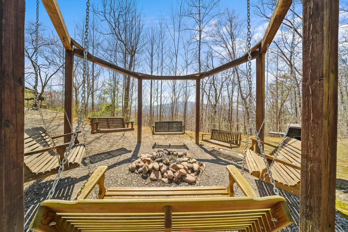 An inviting outdoor gathering area featuring a swing set under tall trees and a cozy fire pit, surrounded by open space for children to play and families to socialize. The natural setting encourages group activities and fosters togetherness.