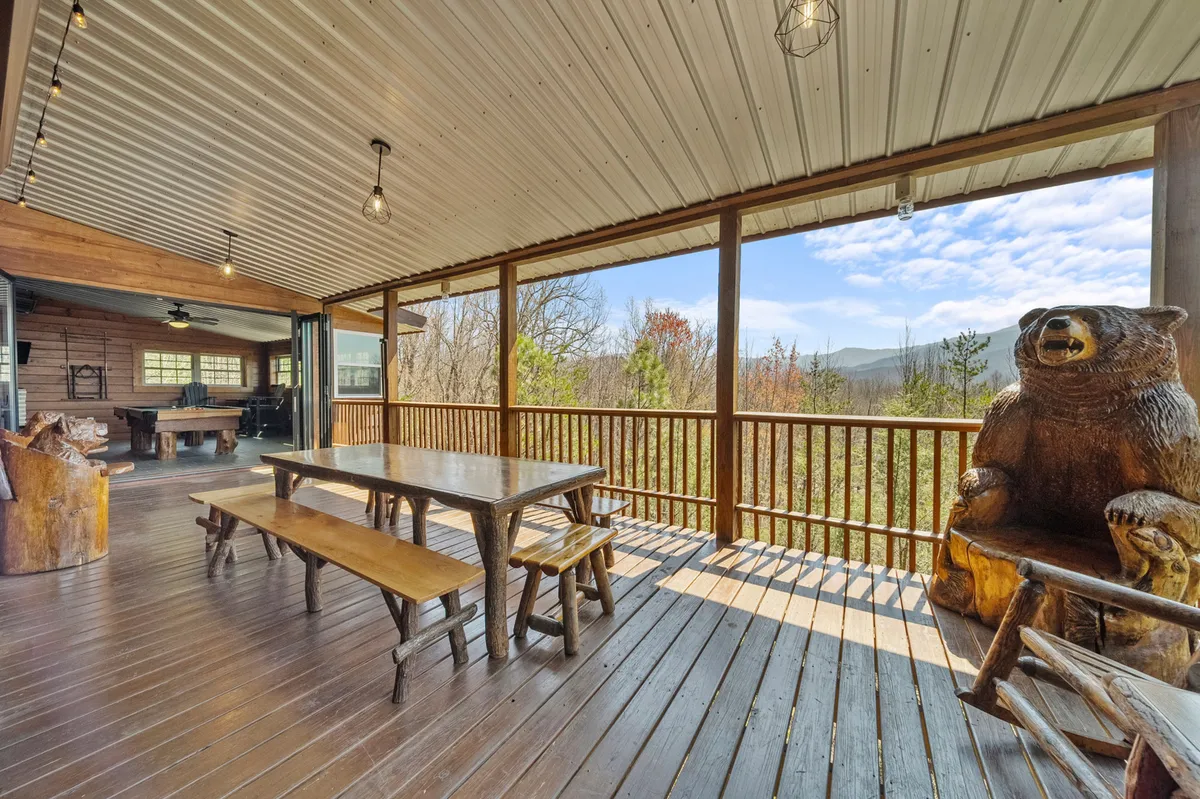A wooden outdoor dining table set on the deck, accompanied by a whimsical bear sculpture and vistas of the surrounding mountains. The environment feels relaxed and inviting, suitable for group meals or quiet sunset moments.