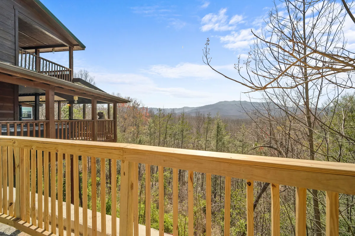 A tranquil porch view overlooks a beautiful mountain landscape, with wooden railings and lush trees surrounding the cabin. The scene invites guests to enjoy their morning coffee, watch for wildlife, or simply breathe in the calm mountain air.