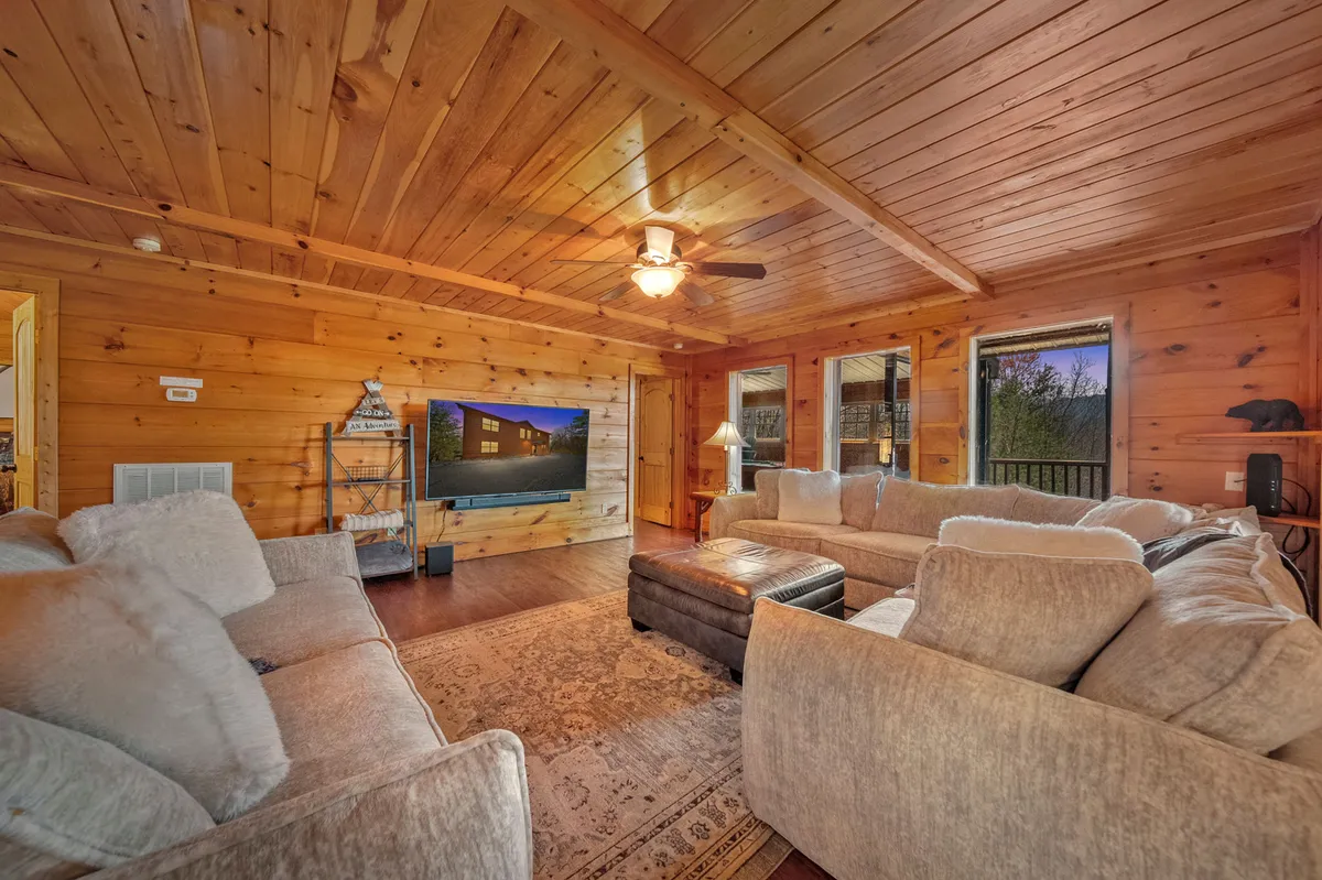 This image captures a cozy, open living area dominated by a large, plush sectional sofa facing a big screen TV. Warm wood accents and large windows allow natural light to pour in, creating an inviting atmosphere perfect for group relaxation and movie nights.